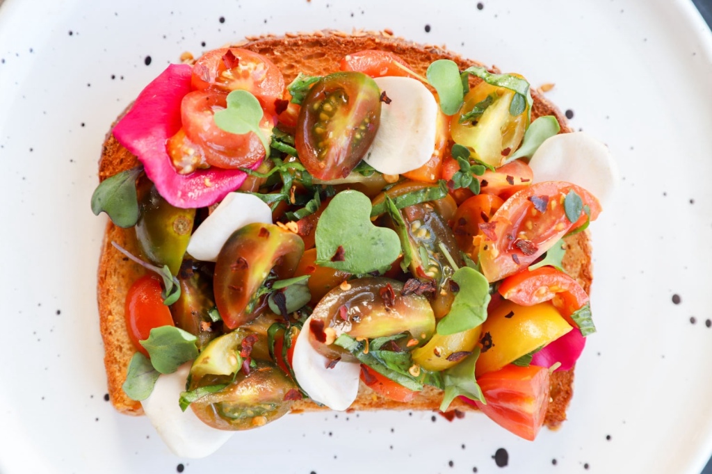 Garden toast topped with edible flowers, tomato slices, and basil leaves