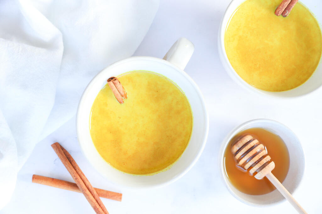 Cup of Golden Moon Milk with a spoon and turmeric