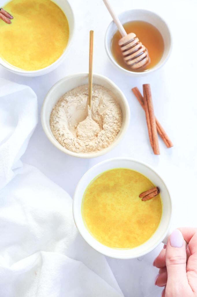 A cup of Golden Moon Milk surrounded by turmeric and ginger