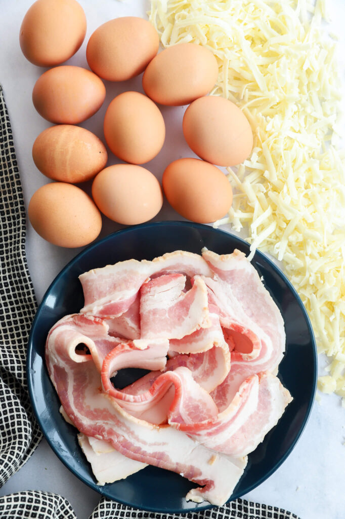 Overhead shot of ingredients for bacon and gruyere egg bites including eggs, bacon, and gruyere cheese