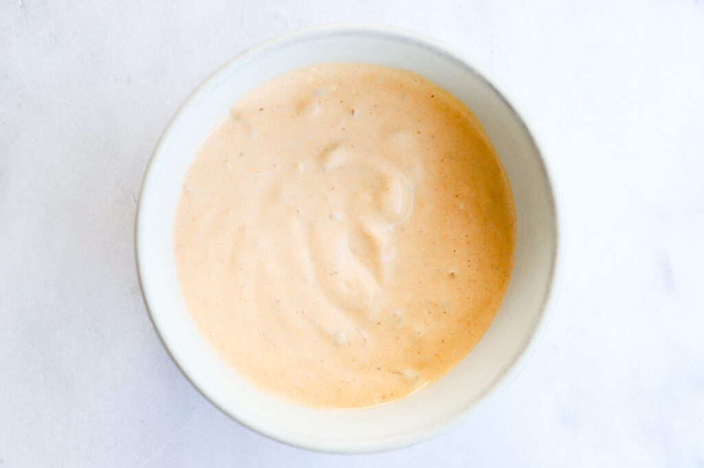 A bowl of chipotle Greek yogurt sauce next to fresh ingredients.