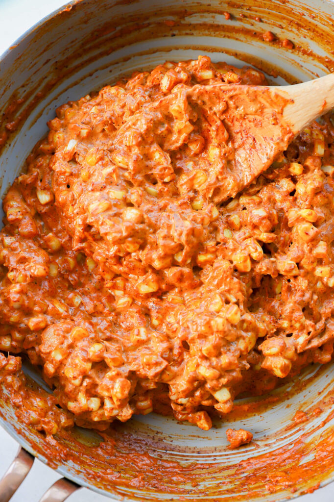 Roasted corn being mixed with cheese and spices for Mexican street corn dip.