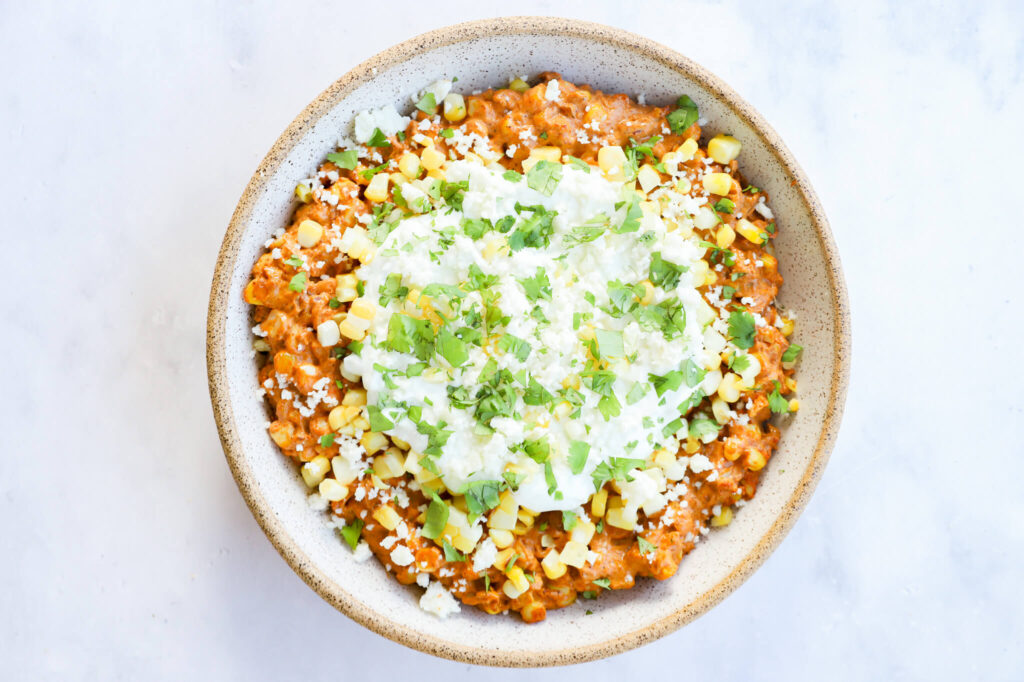 Mexican street corn dip in a bowl, garnished with cilantro, lime, and cheese.