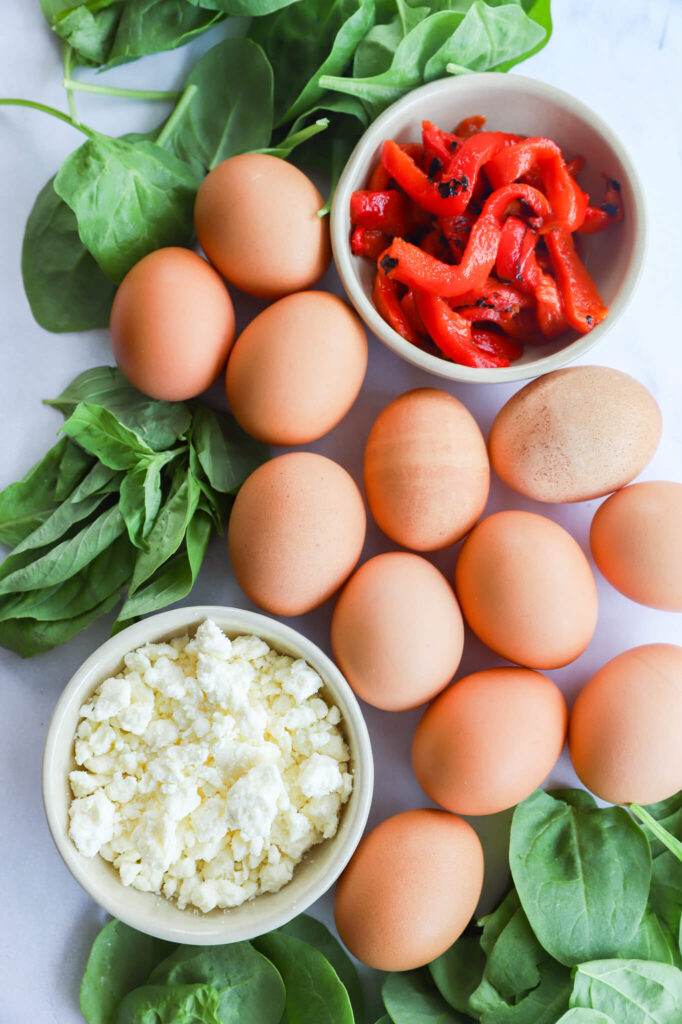 Overhead shot of ingredients for spinach feta egg white bites: egg whites, fresh spinach, and feta cheese.