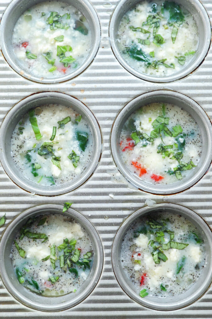 Spinach and feta egg white mixture in a muffin tin, ready to be baked.