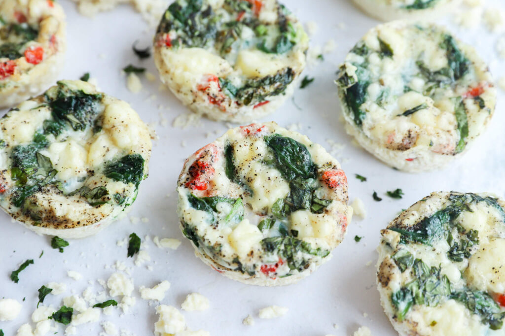 Spinach and feta egg white bites arranged on a serving board with fresh spinach and feta crumbles.